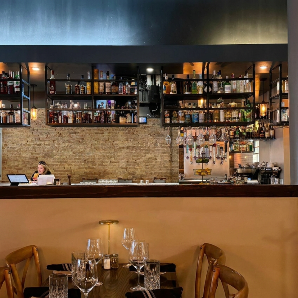 Warmly lit restaurant interior with a fully set dining table, exposed brick wall, and liquor-lined bar shelves behind it.